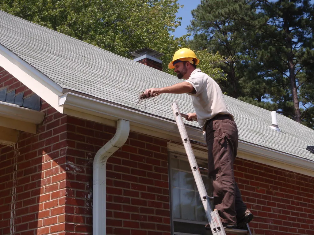 Man on a ladder cleaning gutters on a brick house