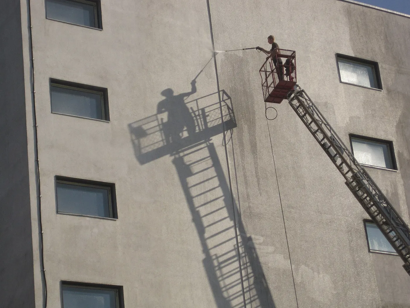 Worker on a lift pressure washing a building wall